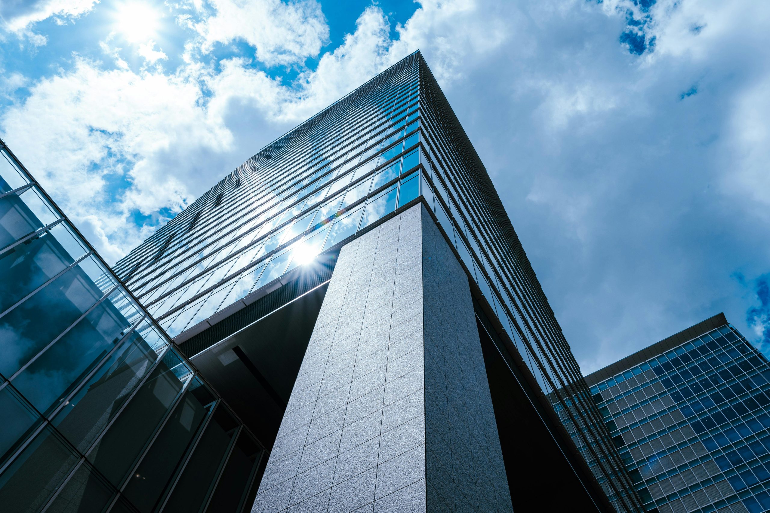 A striking view of a modern skyscraper in Tokyo with sun reflecting on glass under a vibrant blue sky.