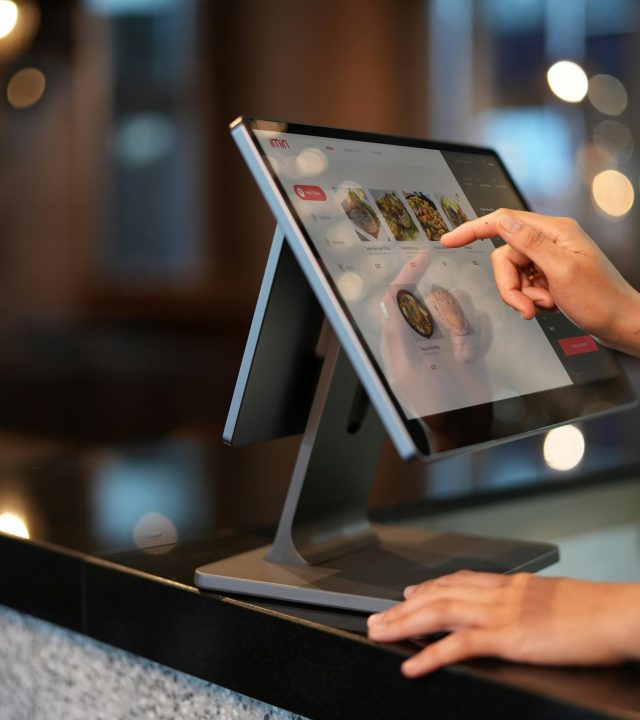 Close-up of a hand interacting with a touchscreen POS system in a restaurant setting.